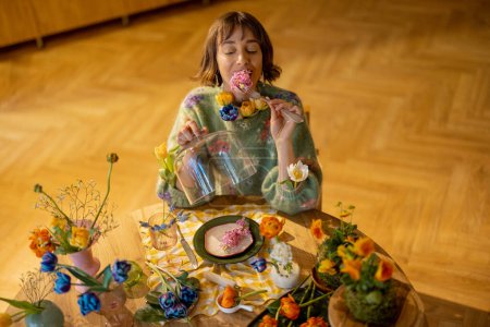 Foto de Mujer joven tiene una cena con flores, sentado junto a la mesa lleno de diferentes flores en jarrones y plato como una comida. Concepto de belleza y dieta floral - Imagen libre de derechos