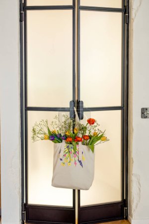 Foto de Bolso de mano con flores frescas cortadas colgando en la puerta de cristal en el interior - Imagen libre de derechos
