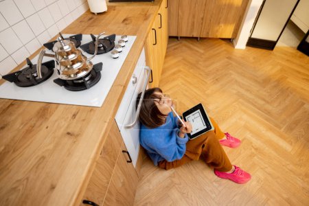 Photo for Creative woman works on digital tablet while sitting on a kitchen floor, view from above. Concept of interior design and remote work from home - Royalty Free Image