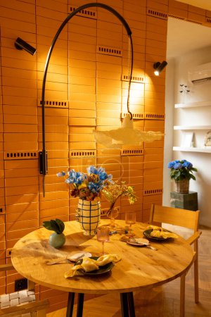 Photo for Sunny and cozy studio apartment with the suns rays passing by the shutters. View on wooden dining table decorated with flowers - Royalty Free Image