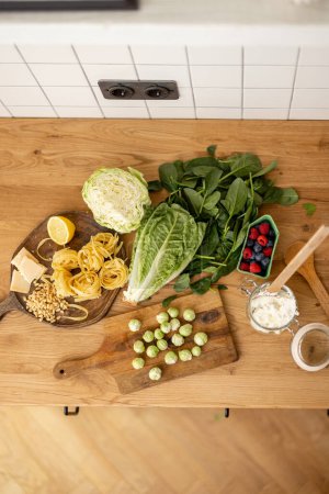 Téléchargez les photos : Ingrédients alimentaires bruts pour la préparation de pâtes végétariennes sur un plateau en bois. Feuilles d'épinards, pousses de brocoli, chou, salade et baies - en image libre de droit