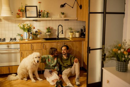 Téléchargez les photos : Jeune couple assis détendu avec un chien mignon sur la cuisine à la maison. Confort à la maison et style de vie domestique concept - en image libre de droit