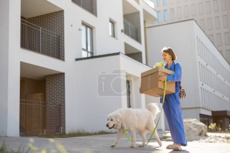 Foto de Mujer llevando cajas de cartón, paseando con su perro al apartamento en un edificio nuevo. Concepto de reubicación, nueva sucesión o entrega - Imagen libre de derechos