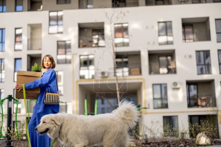 Téléchargez les photos : Femme portant des boîtes en carton, marchant avec son chien à l'appartement à la cour du nouvel immeuble. Concept de déménagement, de nouvelle succession ou de livraison - en image libre de droit