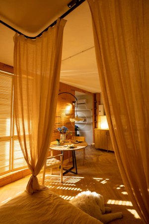 Photo for Sunny and cozy studio apartment with the suns rays passing by the shutters. Interior made in warm tones with natural materials - Royalty Free Image