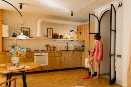 Foto de Moderno apartamento tipo estudio, con vistas a la amplia cocina en tonos beige. Mujer que viene a casa y se para en la puerta - Imagen libre de derechos