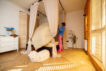 Téléchargez les photos : Femme fait un lit tout en faisant des tâches ménagères dans une chambre confortable avec chien dormant devant - en image libre de droit