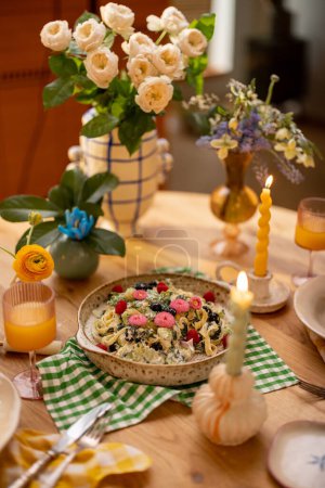 Téléchargez les photos : Pâtes savoureuses aux épinards et aux baies décorées de fleurs comestibles sur une assiette à partager sur une table à manger magnifiquement servie - en image libre de droit