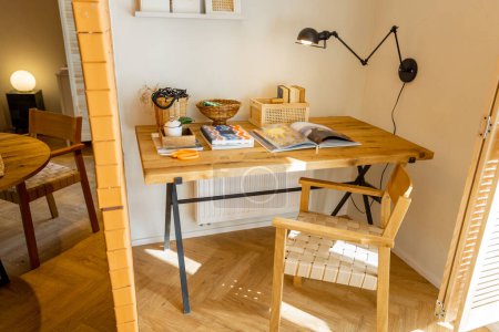 Téléchargez les photos : Vue intérieure de l'espace de travail avec table en bois, étagères avec livres et lampe dans un studio élégant - en image libre de droit