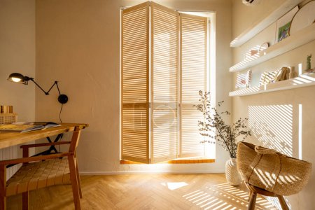 Foto de Vista interior del espacio de trabajo con mesa de madera y silla cerca de la ventana con persianas en elegante apartamento estudio - Imagen libre de derechos