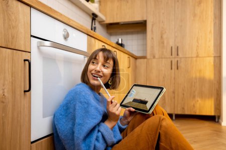 Foto de Mujer diseñando el interior de la cocina en una tableta digital mientras está sentado en el piso de una cocina en un apartamento nuevo. Concepto de diseño interior fácil utilizando dispositivos digitales - Imagen libre de derechos