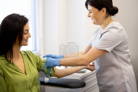 Téléchargez les photos : L'infirmière principale fait un test sanguin veineux dans le bras d'une jeune femme en laboratoire. Travailleur médical pansements de la main avec garrot avant de prendre du sang - en image libre de droit
