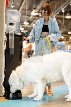 Foto de Mujer dando de beber para su enorme perro de bebedor automático en el supermercado. Amistad y cuidado del concepto de mascotas - Imagen libre de derechos