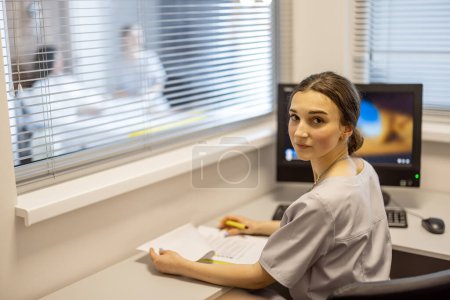 Photo for Young nurse sits in inspection room of medical ward, monitoring the health of patients. Concept of nursing and medical support - Royalty Free Image