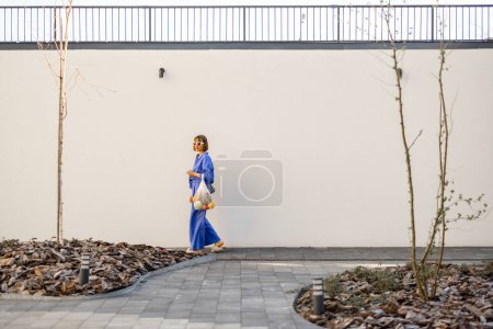 Foto de Mujer en pijama azul camina con bolsa de malla llena de frutas frescas en fondo blanco de la pared al aire libre. Concepto de sostenibilidad y estilo de vida moderno - Imagen libre de derechos