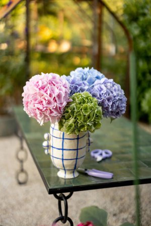Foto de Beautiful bouquet of colorful hydrangea flowers in vase on table in garden - Imagen libre de derechos