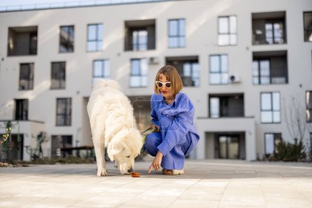 Foto de La mujer señala con el dedo la caca de los perros, mientras camina con su mascota en el patio de un edificio de apartamentos. Concepto de limpieza después de mascotas en lugar público - Imagen libre de derechos