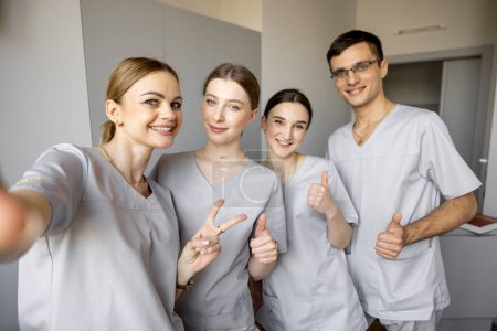 Téléchargez les photos : Jeune équipe d'infirmières faisant des photos selfie, tout en se tenant ensemble dans le service médical. Portrait d'infirmières gaies en clinique - en image libre de droit