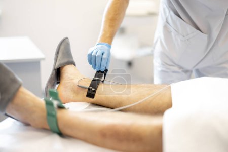 Téléchargez les photos : Cardiologue fait un cardiogramme, accrochant des contacts aux jambes d'un patient d'âge moyen à la clinique, gros plan - en image libre de droit