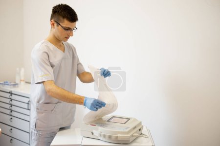 Foto de Cardiólogo joven imprimiendo cardiograma en una máquina de cardiografía portátil en la clínica - Imagen libre de derechos