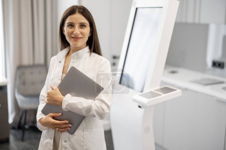 Téléchargez les photos : Portrait d'un médecin debout près de la machine à analyser le corps au salon de beauté. Concept de recherche corporelle non invasive et rapide pour l'industrie de la beauté - en image libre de droit
