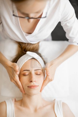 Téléchargez les photos : Esthéticienne fait massage professionnel du visage pour le visage des femmes au salon de beauté. Jeune femme caucasienne adulte recevant massage facial relaxant - en image libre de droit