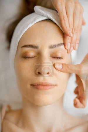 Photo for Adult woman receiving relaxing facial massage, close-up top view on womans face during a massage. Massaging the area under eyes - Royalty Free Image