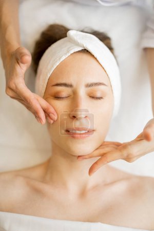 Photo for Adult woman receiving relaxing facial massage, close-up view from above on womans face during a massage. Beautiful pose of masseurs fingers - Royalty Free Image