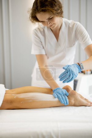 Photo for Young worker of a beauty salon during hair removal procedure on a womans legs. Depilation concept and beauty procedures - Royalty Free Image