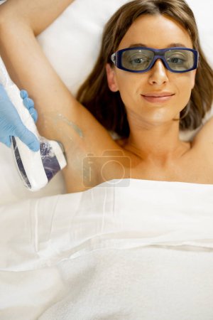 Photo for Young woman during hair removal procedure on her armpits at beauty salon. Laser epilation and skin care concept - Royalty Free Image