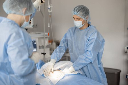Téléchargez les photos : Les chirurgiens se préparent à l'opération, couvrant le patient d'une usure stérile. Concept de stérilité pendant le traitement chirurgical et la procédure invasive - en image libre de droit