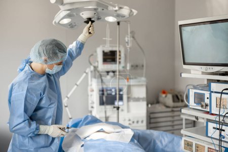 Téléchargez les photos : Le chirurgien installe une lumière, se préparant à l'intervention invasive dans la salle d'opération. Concept de traitement chirurgical - en image libre de droit