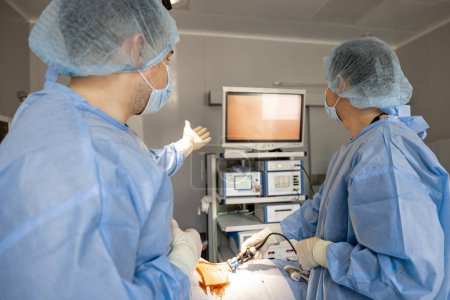 Téléchargez les photos : Deux chirurgiens effectuent une intervention mini-invasive avec endoscopes, en regardant le moniteur dans la salle d'opération. Concept de traitement endoscopique assisté par ordinateur - en image libre de droit