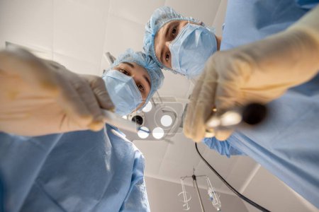 Foto de Cirujanos confiados mirando a la cámara mientras operan a un paciente. Idea de cirugía y tratamientos invasivos - Imagen libre de derechos