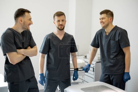 Photo for Council of three young and cheerful surgeons in a medical office. Concept of teamwork and professional medical treatment - Royalty Free Image