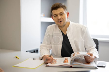 Photo for Portrait of vascular surgeon sitting with a book in medical office. Concept of portraits of real doctors - Royalty Free Image