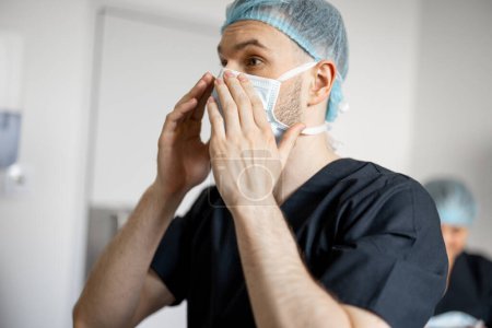 Photo for Surgeon wearing facial mask in preparation for a surgical operation. Concept of sterility and surgery - Royalty Free Image