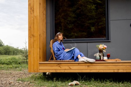 Photo for Woman resting on beautiful terrace of a wooden cottage on nature. Escaping to nature, calm and relaxation concept - Royalty Free Image