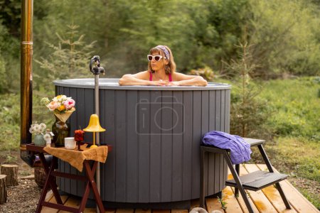Photo for Young woman bathing in hot tub heated by firewood, resting in the mountains. Concept of recreation and spa procedures on nature - Royalty Free Image