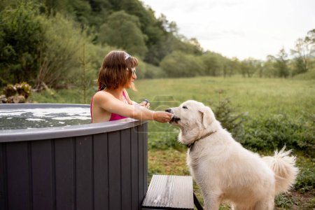 Foto de Mujer bañándose en bañera de hidromasaje al aire libre mientras descansa con su lindo perro en casa en las montañas. Concepto de recreación y pasar tiempo libre con mascotas en la naturaleza - Imagen libre de derechos