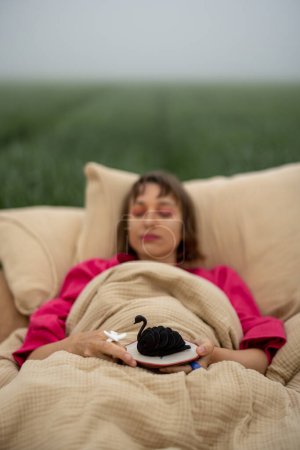 Téléchargez les photos : Femme aime dessert sucré tout en étant couché sur le lit à l'extérieur. Passer la matinée dans des draps souples sur un champ vert. Concept de rêves doux - en image libre de droit