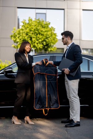 Photo for Female chauffeur gives a businessman his suit, after a business trip in luxury taxi. Concept of personal assistant, driver and business transportation service - Royalty Free Image