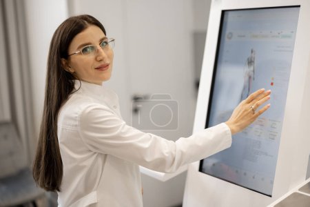 Photo for Portrait of a doctor touching the screen of body analyzer machine at beauty salon. Concept of modern technologies in medicine and beauty industry - Royalty Free Image