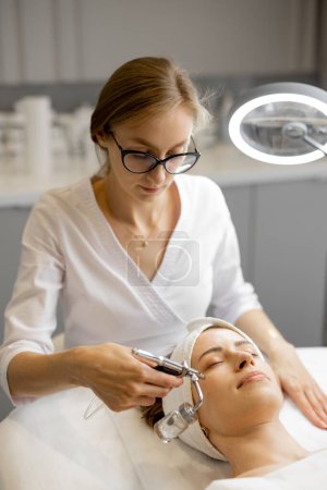 Foto de Joven cosmetólogo realiza mesoterapia de oxígeno en la cara de las mujeres en el salón de belleza. Concepto de tratamiento no invasivo y revitalizante de la piel - Imagen libre de derechos