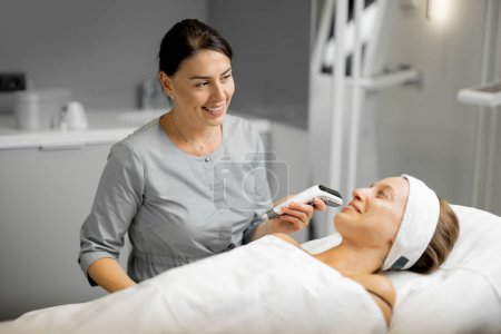 Photo for Cosmetologist with a woman client during consultation before beauty procedure with dermapen - Royalty Free Image