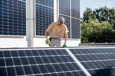Foto de Hombre instalando paneles solares en el techo de su casa, atornillando la celda en la azotea plana para el autoconsumo. Concepto de energía renovable y sostenibilidad - Imagen libre de derechos