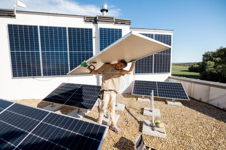 Téléchargez les photos : L'homme porte un panneau solaire sur ses épaules tout en installant la plante solaire d'un toit de sa propriété. Le concept des énergies renouvelables pour l'autoconsommation. Idée d'installation de panneaux pour les ménages - en image libre de droit