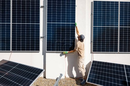 Foto de Hombre instalando paneles solares en la pared vertical en una azotea de su casa para el autoconsumo. Concepto de energía renovable y sostenibilidad - Imagen libre de derechos