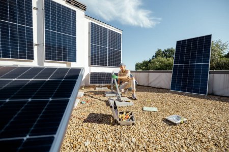 Photo for Man installs mounts for solar panels on a rooftop of household. Owner of property installing solar panels for self consumption - Royalty Free Image