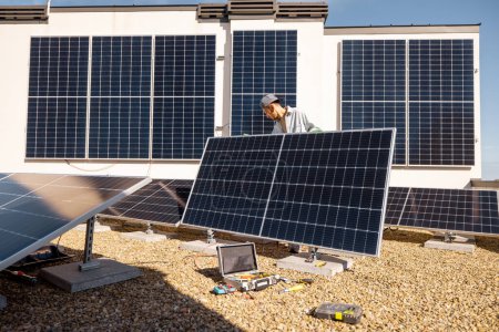 Foto de Hombre instalando paneles solares en el techo de su casa, ajustando la celda en la azotea plana para el autoconsumo. Concepto de energía renovable y sostenibilidad - Imagen libre de derechos